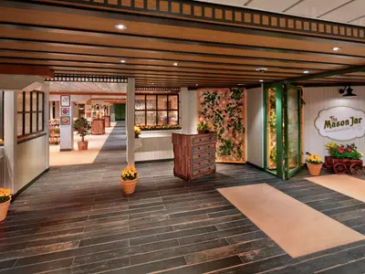 Wonder of the Seas: Ansicht des 'The Mason Jar' Restaurants. Holzfußboden, Deckenbalken, Pflanzen, eine Kommode und der rustikal dekorierte Eingangsbereich sind zu sehen.
