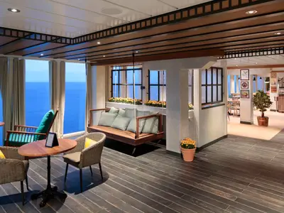 Innenansicht eines Lounge-Bereichs der Wonder of the Seas. Große Fenster bieten Meerblick, dazu dunkler Holzboden, Sitzgruppen und ein Hängesofa. Im Hintergrund ein Buffetbereich.