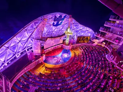 Das nächtliche AquaTheater der Wonder of the Seas: Publikum, Wassershow, lila-blaue Beleuchtung und markante Dachkonstruktion.
