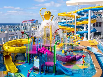 Der farbenfrohe Wasserpark auf dem Deck der Wonder of the Seas bietet mehrere gelbe und blaue Rutschen, einen Kippeimer und bunte Wasserspiele. Im Hintergrund ist das offene Meer sichtbar.