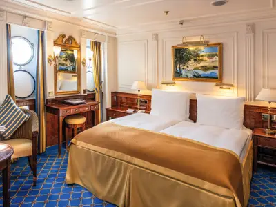 Blick in eine elegante Außenkabine an Bord der Sea Cloud II mit edlem Holzdekor, Doppelbett und Schminktisch.