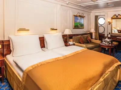 Luxuriöse Außenkabine an Bord der Sea Cloud II mit Doppelbett, Sitzecke, Schminktisch und Ochsenaugen-Bullauge.