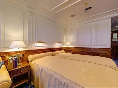 Blick in eine elegante Kabine an Bord der Sea Cloud Ii mit zwei Betten, warmem Holz und edler Wandvertäfelung.