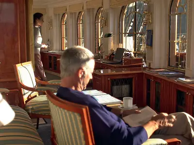 Ein Passagier liest in einem Sessel in der elegant eingerichteten Bibliothek an Bord der Sea Cloud Ii.