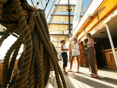 Drei sommerlich gekleidete Frauen unterhalten sich mit Getränken auf dem Teakdeck an Bord der Sea Cloud II.