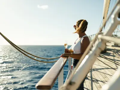 Eine Frau mit Sonnenbrille blickt an Deck der Sea Cloud II mit einem Sektglas auf das weite blaue Meer.