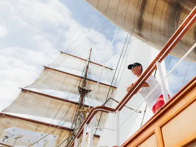 Ein Mann mit Sonnenbrille lehnt an der Reling der Sea Cloud II und blickt zu den imposanten Masten und Segeln.