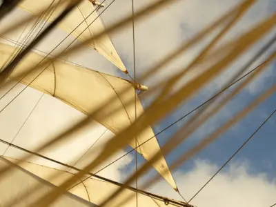 Blick durch Taue und Takelage hinauf zu den blähenden weißen Segeln des Großseglers Sea Cloud II vor blauem Himmel.