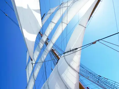Froschperspektive auf die blähend gefüllten weißen Segel, Masten und Seile der Sea Cloud II vor blauem Himmel.