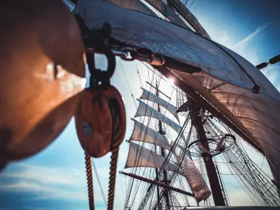 Blick von Deck der Sea Cloud II in die sonnendurchflutete Takelage mit Holzblöcken, Tauwerk und Segeln.