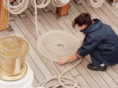 Auf dem Holzdeck der Sea Cloud Ii kniet eine Person und legt ein langes Schiffstau akkurat in einer Spirale auf.
