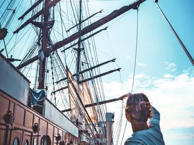Eine Person blickt vom Deck der Sea Cloud Ii hinauf zu den Masten, Segeln und der beeindruckenden Takelage.