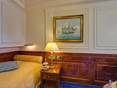 Klassisch eingerichtete Kabine an Bord der Sea Cloud Ii mit Einzelbett, Holzvertäfelung, Tischlampe und Schiffsgemälde.