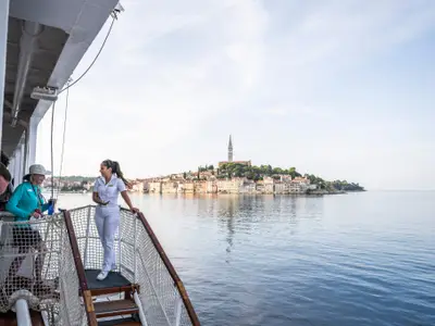 Eine Offizierin im Gespräch mit Gästen auf dem Deck der Sea Cloud II vor der Kulisse von Rovinj.