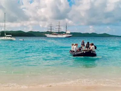 Ein Tenderboot bringt Passagiere der Sea Cloud II an den Strand, während der Großsegler im Hintergrund ankert.