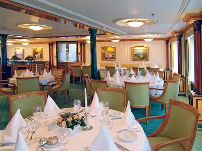 Das klassisch eingerichtete Restaurant an Bord der Sea Cloud II mit feinen Tischgedecken und grünen Sesseln.