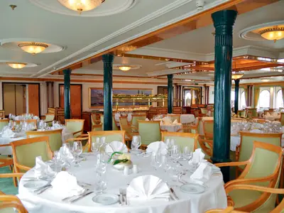 Elegantes Restaurant an Bord der Sea Cloud Ii mit stilvoll eingedeckten runden Tischen und grünen Säulen.