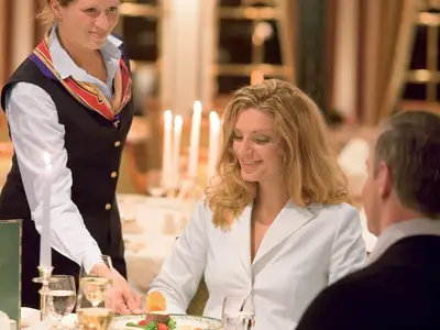 Eine lächelnde Frau wird im stimmungsvoll beleuchteten Restaurant an Bord der Sea Cloud Ii von der Crew bedient.