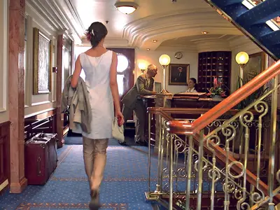 Eine Frau geht durch den Rezeptionsbereich mit eleganter Messingtreppe an Bord der Sea Cloud II.