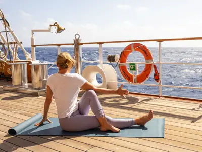 Eine Frau sitzt auf einer Gymnastikmatte auf dem Teakdeck der Sea Cloud II und macht Yoga mit Blick aufs Meer.