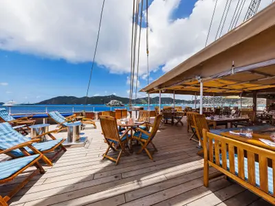 Ein weitläufiges Holzdeck an Bord der Sea Cloud II mit blauen Liegestühlen, Holztischen unter einem Sonnendach und Blick aufs Meer.
