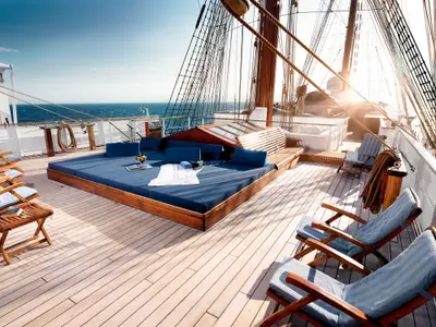 Sonnendeck an Bord der Sea Cloud Ii mit großen blauen Liegekissen, Liegestühlen aus Holz und Blick auf das Meer.