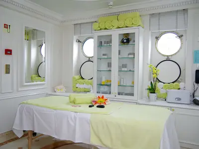 Heller Behandlungsraum im Spa-Bereich an Bord der Sea Cloud Ii mit Massageliege, gelben Handtüchern und Produktvitrine.