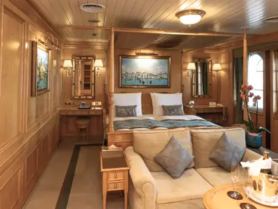 Geräumige Suite an Bord der Sea Cloud II mit Holzwänden, Himmelbett, gemütlicher Couch und kunstvollen Gemälden.