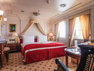 Klassisch eingerichtete Suite an Bord der Sea Cloud II mit rotem Doppelbett, Baldachin und Holzmöbeln.
