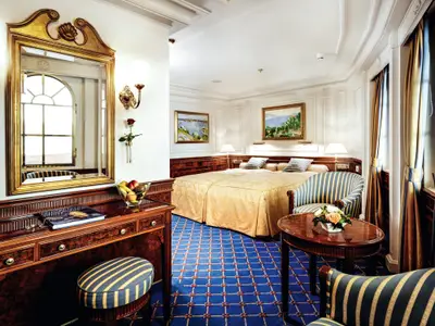 Luxuriös eingerichtete Suite an Bord der Sea Cloud Ii mit Doppelbett, Frisiertisch und blauem Teppich.