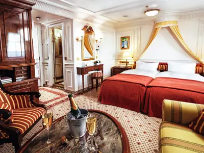 Elegante Junior Suite an Bord der Sea Cloud Ii mit Doppelbett, Baldachin, Schminktisch und Sektkühler im Vordergrund.