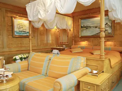 Luxuriös eingerichtete Suite an Bord der Sea Cloud II mit edler Holzverkleidung, großem Himmelbett und gelber Sitzecke.