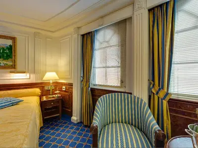 Klassisch eingerichtete Suite an Bord der Sea Cloud Ii mit blau-gelbem Sessel, großem Bett und Holzvertäfelung.