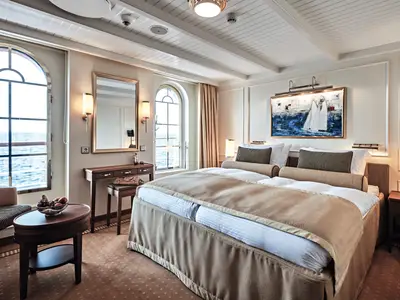 Geräumige Außenkabine an Bord der Sea Cloud Spirit mit großem Doppelbett, Schminktisch und Bogenfenstern mit Meerblick.