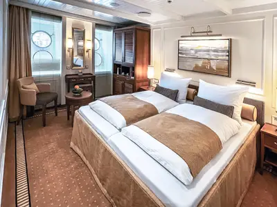 Elegante Außenkabine an Bord der Sea Cloud Spirit mit Doppelbett, Holzschränken, Sessel und warmem Licht.