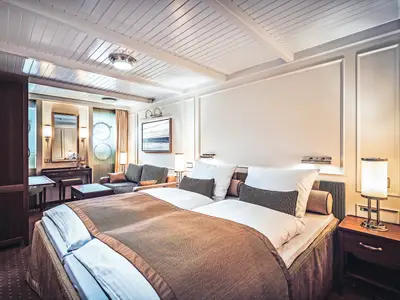 Blick in eine edel eingerichtete Kabine an Bord der Sea Cloud Spirit mit großem Bett, Nachttischlampen und Couch.