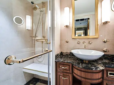 Elegantes Badezimmer in einer Kabine an Bord der Sea Cloud Spirit mit goldenen Armaturen, Waschtisch aus Marmor und Glasdusche.
