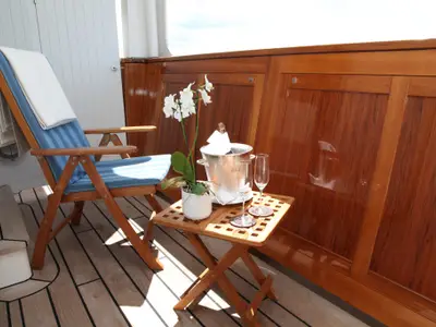 Balkon an Bord der Sea Cloud Spirit mit Holzverkleidung, blau gestreiftem Liegestuhl, Orchidee und Champagner auf einem Beistelltisch.