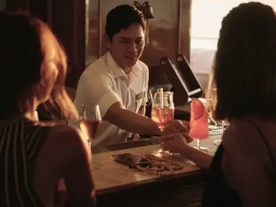 Ein Barkeeper serviert zwei Gästen farbenfrohe Cocktails an einer eleganten Holzbar an Bord der Sea Cloud Spirit.