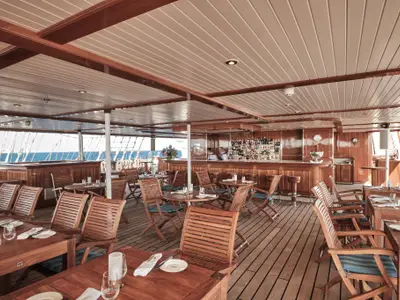 Gedeckte Holztische und eine gut sortierte Bar auf dem überdachten Deck an Bord der Sea Cloud Spirit.