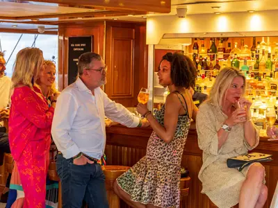 Gäste unterhalten sich gut gelaunt mit Drinks an der holzverkleideten Bar an Bord der Sea Cloud Spirit.