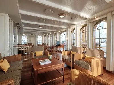 Helles Interieur der Bibliothek an Bord der Sea Cloud Spirit mit gestreiften Sesseln, Holztischen und großen Rundbogenfenstern.