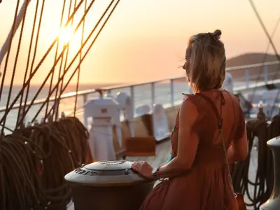 Eine Frau blickt im warmen Abendlicht des Sonnenuntergangs über das Meer an Bord der Sea Cloud Spirit.