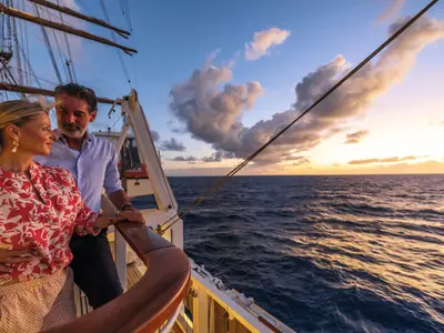 Ein Paar steht am Abend an der hölzernen Reling an Bord der Sea Cloud Spirit und schaut auf den Ozean.