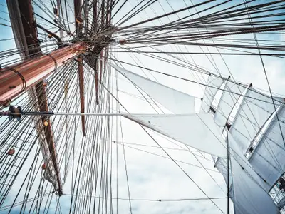Froschperspektive auf den hölzernen Mast, weiße Segel und die aufwendige Takelage an Bord der Sea Cloud Spirit.