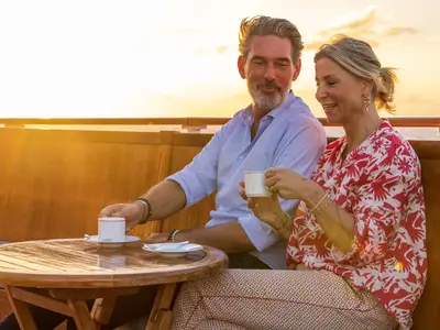 Ein elegantes Paar sitzt bei warmem Sonnenuntergang mit Kaffeetassen an Deck der Sea Cloud Spirit.