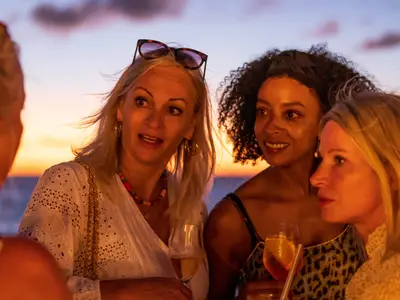 Vier Frauen unterhalten sich gut gelaunt bei Sonnenuntergang mit Cocktails an Deck an Bord der Sea Cloud Spirit.