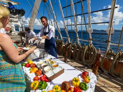 Ein Schiffskoch serviert Speisen am Buffet auf dem Holzdeck der Sea Cloud Spirit auf offener See.