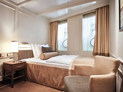 Gemütlich eingerichtete Einzelkabine an Bord der Sea Cloud Spirit mit Einzelbett, Nachttisch, Sessel und Fenstern.