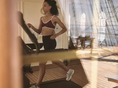 Eine Frau joggt auf einem Laufband im Fitnessraum an Bord der Sea Cloud Spirit mit Blick auf das Holzdeck.
